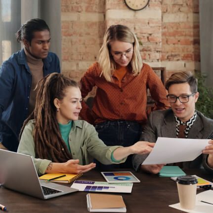 Four colleagues collaborating on a project at a table with papers and laptops.