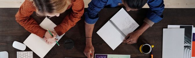 A person holding a pen over a blank notebook on a wooden table.
