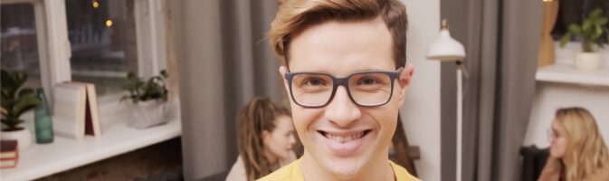 Smiling young man wearing glasses in a casual setting.