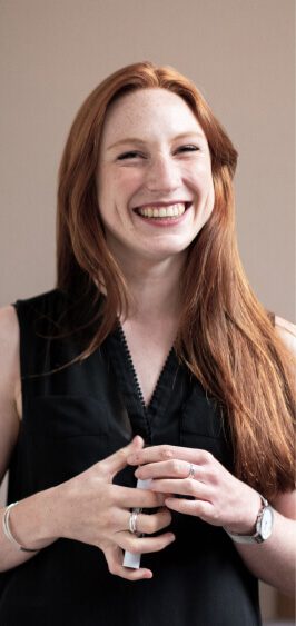 Smiling woman with long red hair wearing a black sleeveless top.