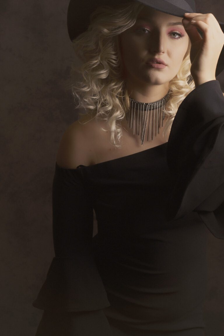 Woman in elegant black dress with curly hair and statement necklace.
