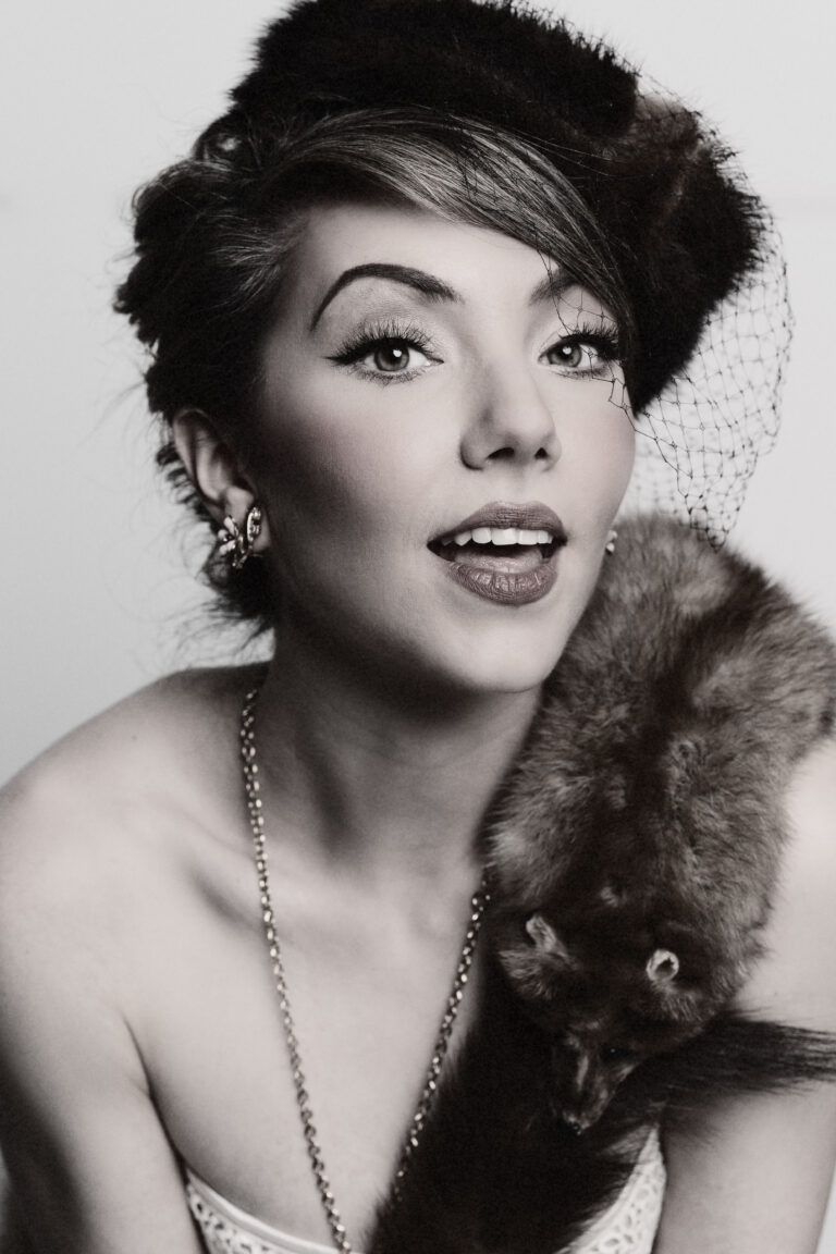 Elegant woman in vintage attire with fur stole and netted hat.