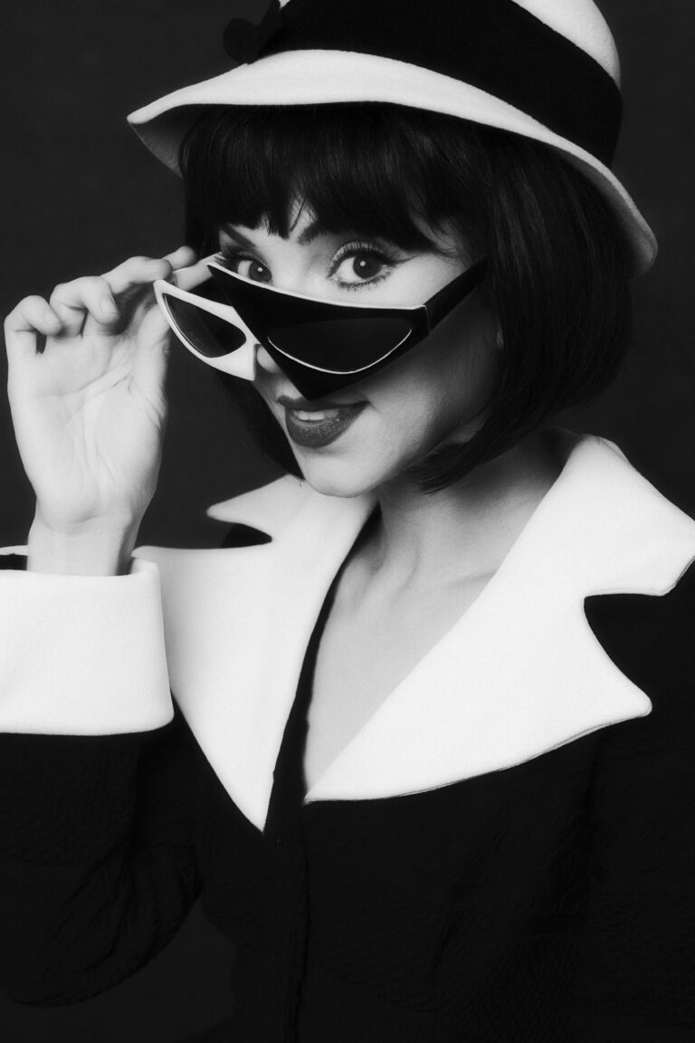 Stylish woman in black and white adjusting her sunglasses with a playful expression.