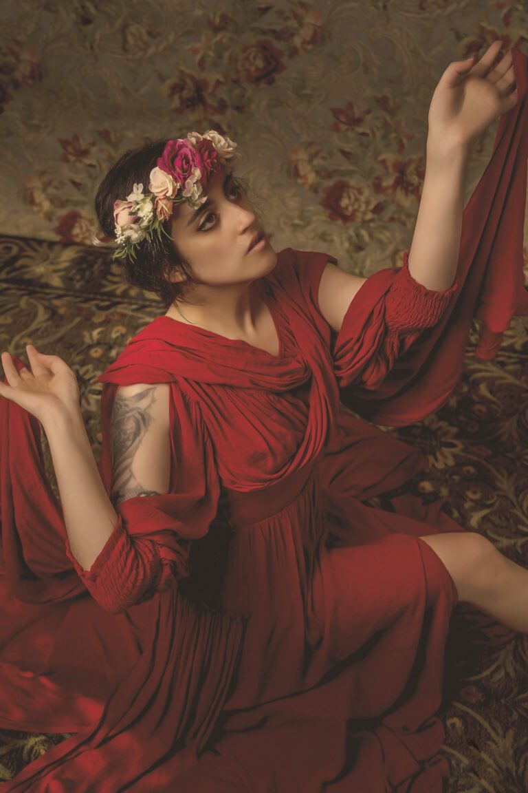 Woman in a red dress with a floral crown, striking a graceful pose.