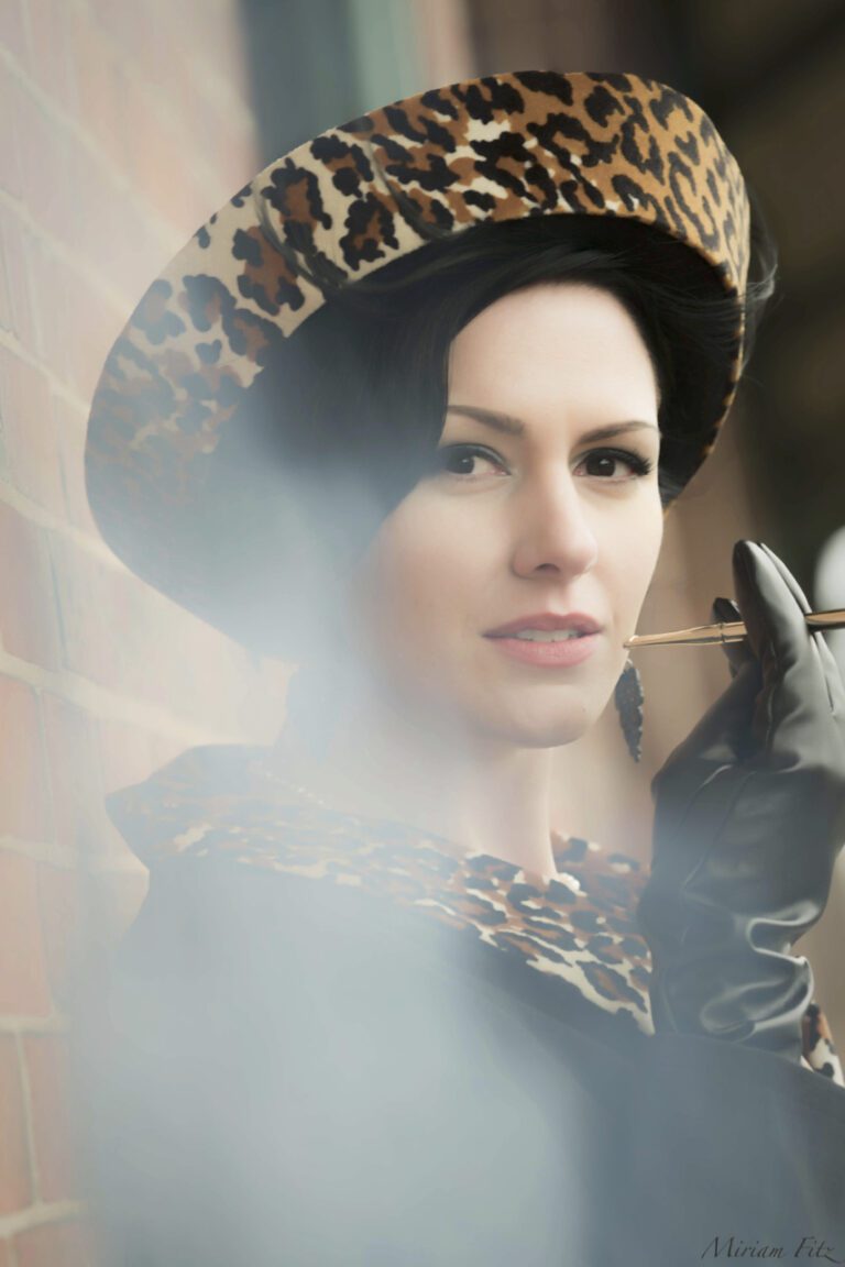 Portrait of a woman in a leopard print coat and hat, holding a cigarette.