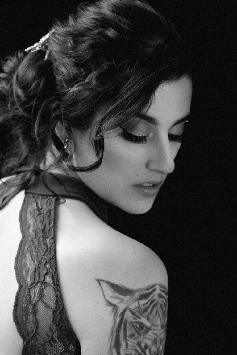 Black and white portrait of a woman with curly hair and a tattoo on her shoulder.