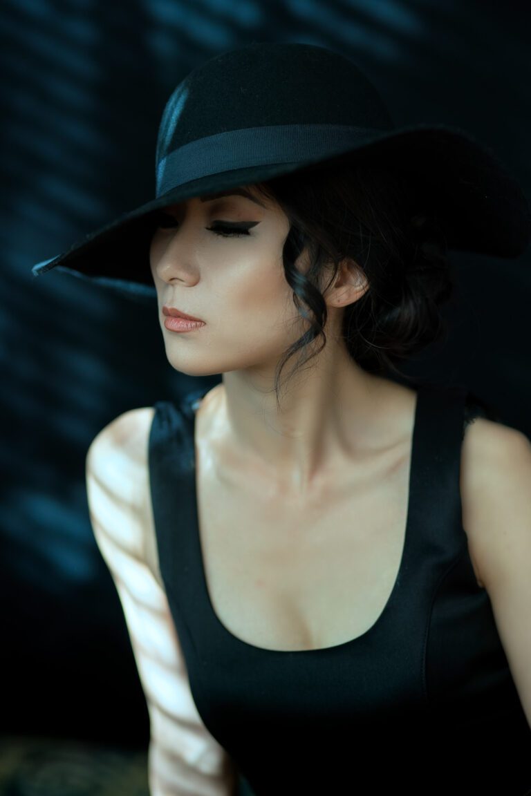 Woman in a black hat and tank top with a contemplative expression.