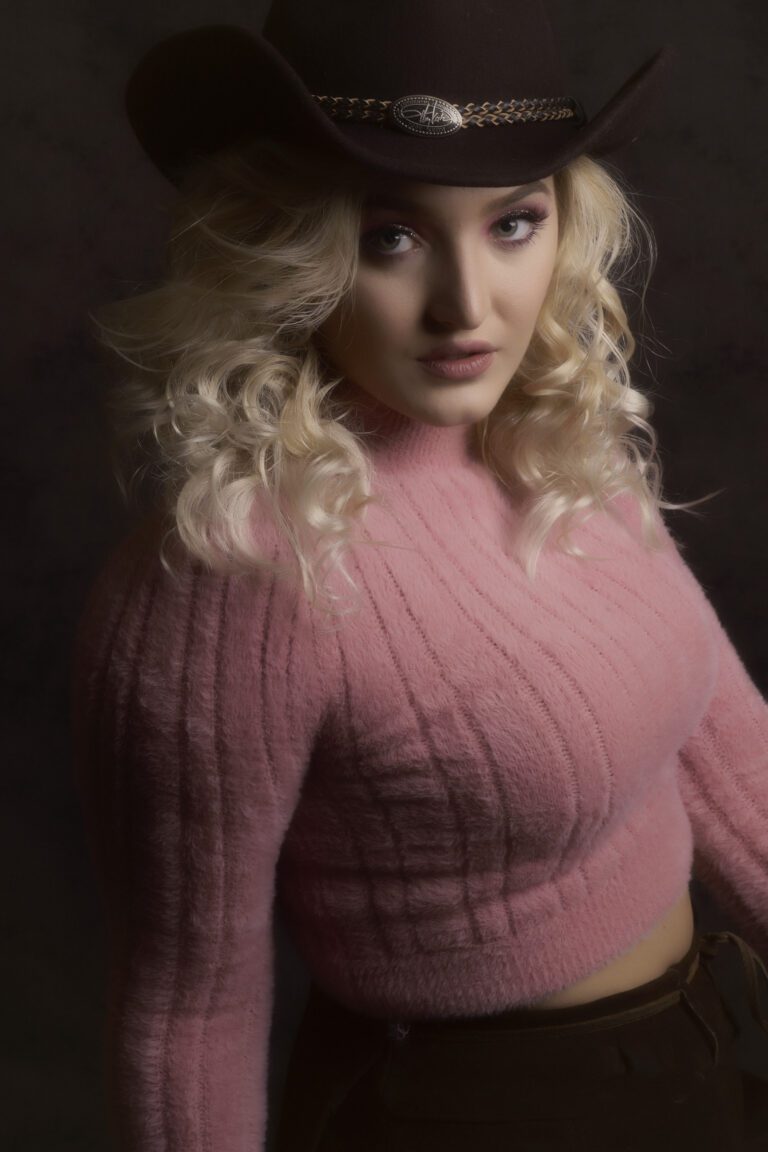 Young woman with curly blonde hair wearing a pink sweater.